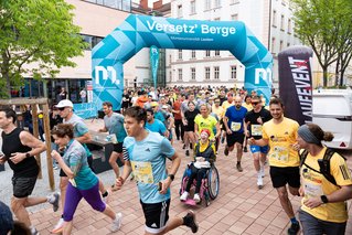 Teilnehmer*innen inklusive einer jungen Frau im Rollstuhl bewegen sich rund um die Startlinie des Wings4life-Laufes.