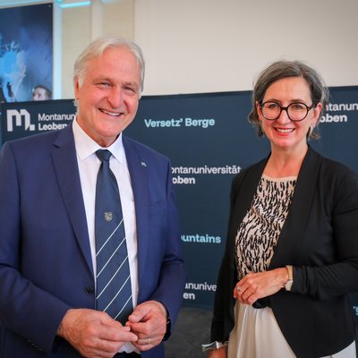 Zwei Personen in formeller Kleidung vor einem Montanuniversität‑Leoben‑Backdrop; links blauer Anzug mit Krawatte, rechts schwarzer Blazer.