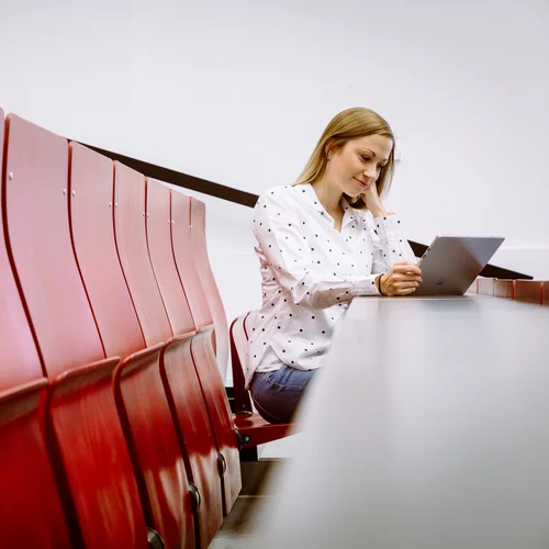 A student sits in the lecture theatre and looks at a laptop.