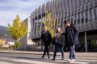 Zwei junge Frauen und ein junger Mann, alle etwa 20 Jahre alt, gehen über einen Zebrastreifen vor dem Erzherzog Johann Gebäude der Montanuniversität Leoben.