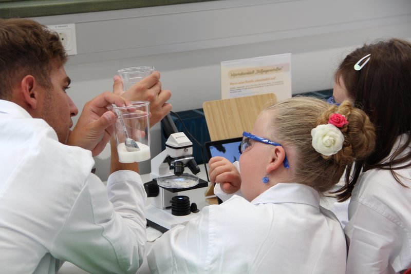 Zwei Mädchen beschäftigen sich gemeinsam mit einem Studenten im Lehr-Lern-Labor am Mikroskop mit dem Rohstoff Salz.