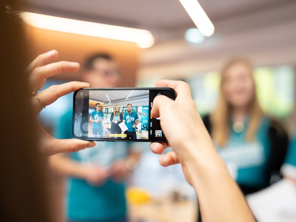 A person takes a photo of the university's motto ‘Glück auf’ with their smartphone.