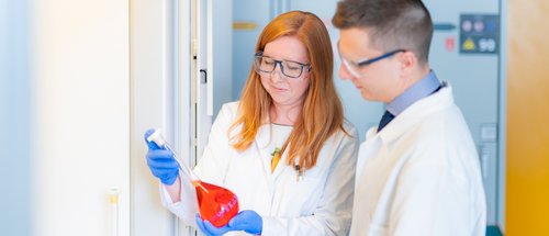Two scientists in the laboratory are analysing a red liquid in a test tube.