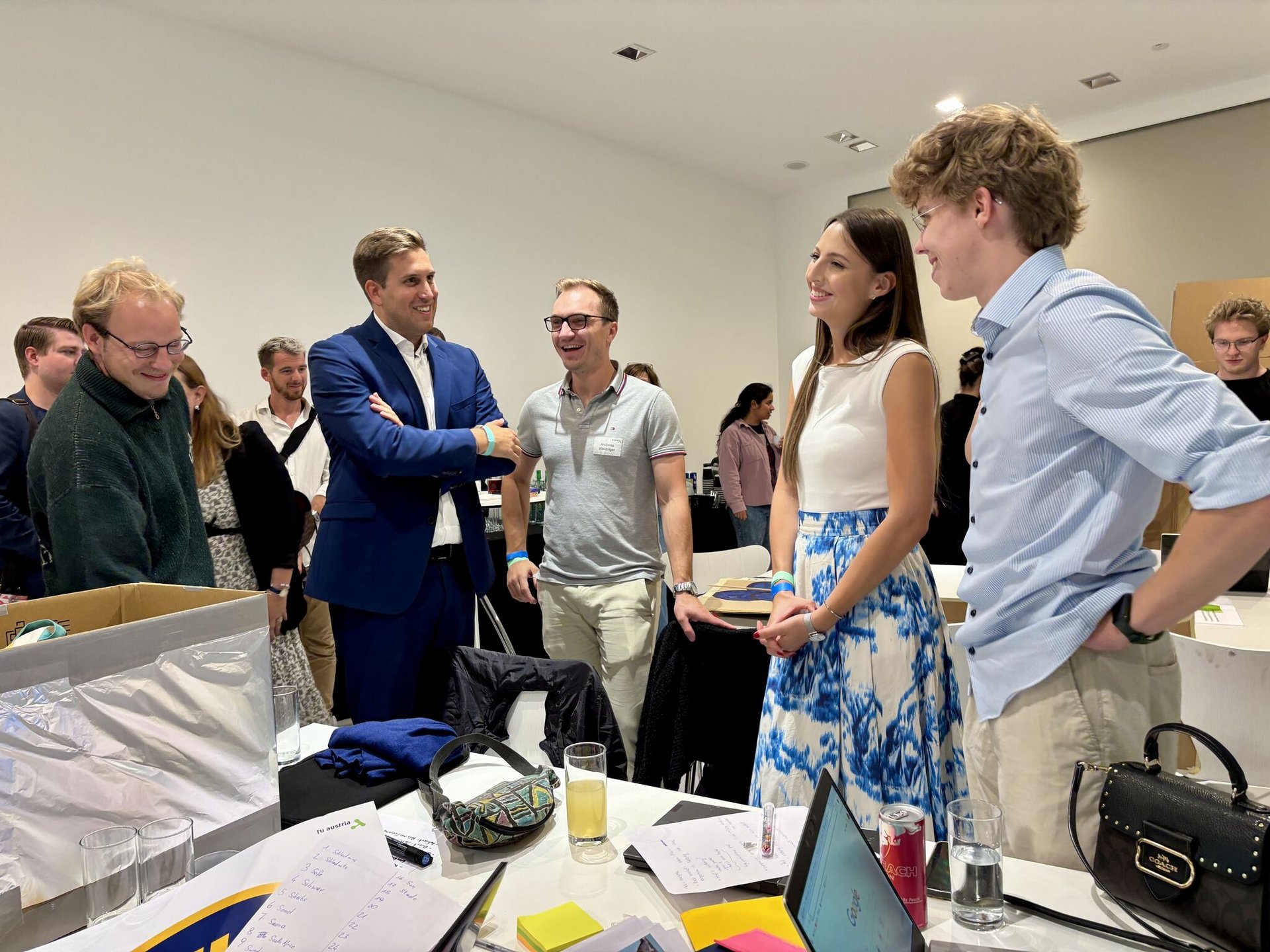 Staatssekretär Alexander Pröll steht im blauen Anzug in mitten einer Gruppe von Studierenden und bespricht ihre Ideen.