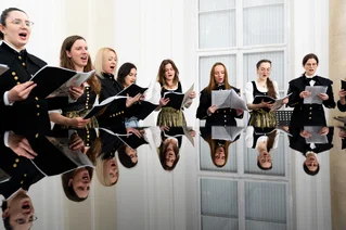 Mitglieder des Hochschulchors stehen um ein Klavier herum und halten ihre Gesangsnotizen in den Händen. Sie singen. 