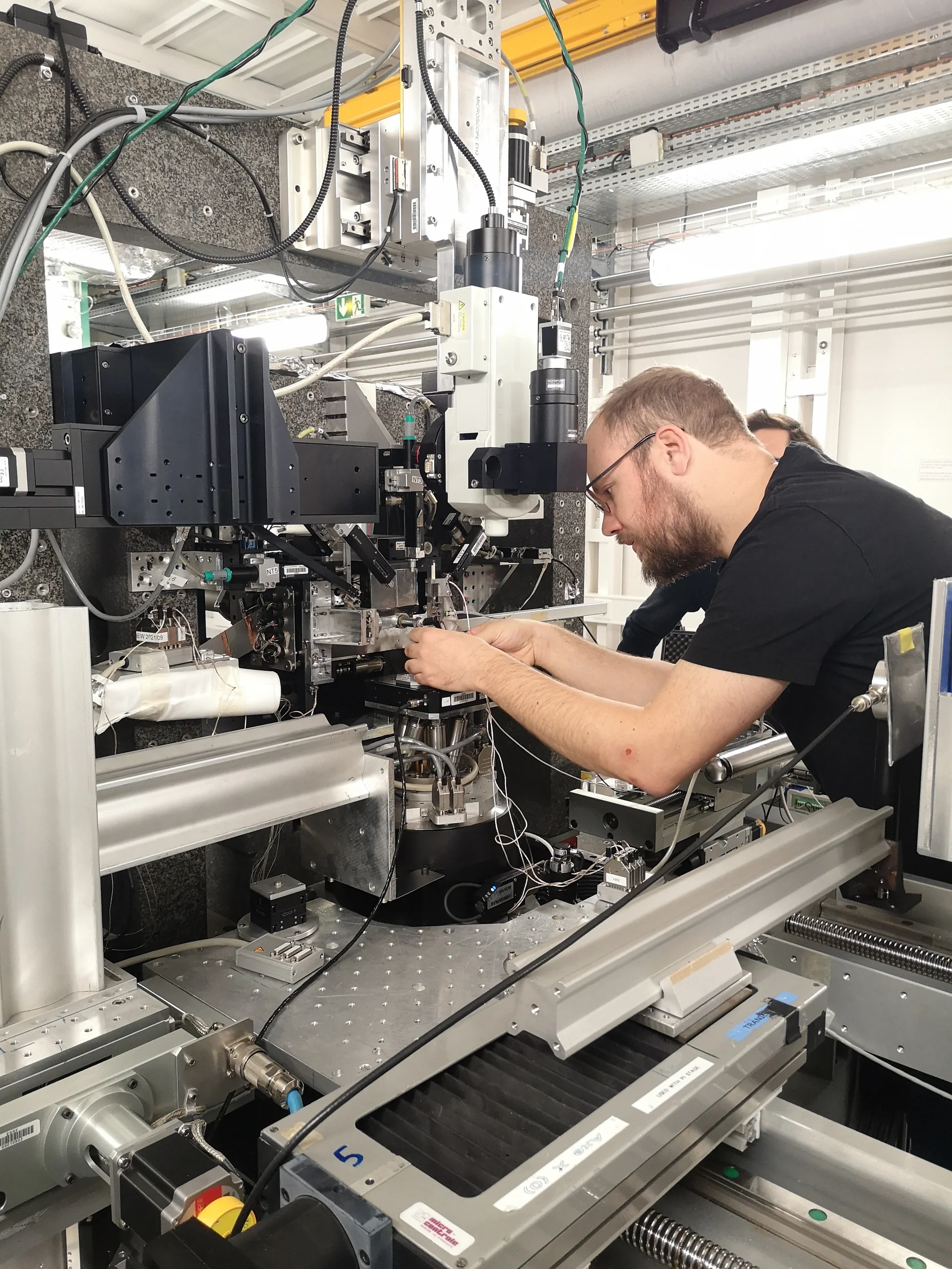 In einem High‑Tech‑Labor arbeitet eine Person konzentriert an einer Experimentierstation mit optischen Modulen, Probenhalter, Motorachsen und zahlreichen Kabeln – typische Ausstattung einer Synchrotron‑Beamline.
