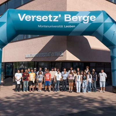 Gruppe vor dem Uni-Gebäude unter einem großen aufblasbaren Torbogen „Versetz’ Berge“ der Montanuniversität Leoben.
