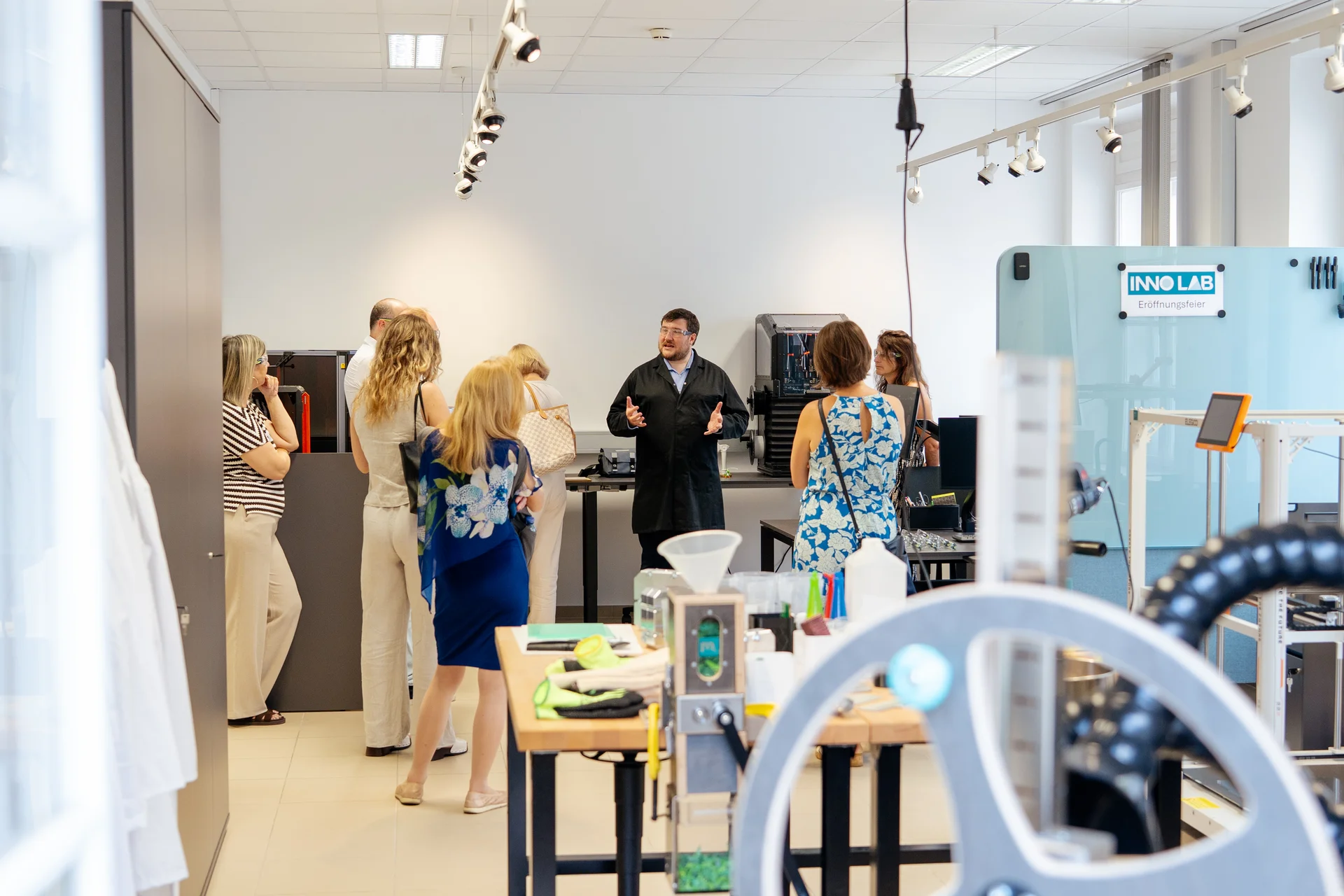 Gruppe bei einer Führung im Innovationslabor: eine Person erklärt, umgeben von Werkbänken, Maschinen und 3D‑Druckern.
