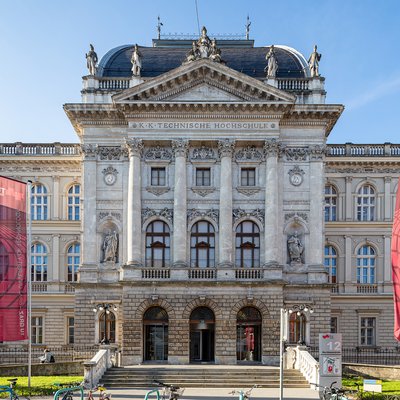 Drei Fahnen wehen an Masten vor einem dreistöckigen, historischen Gebäude.