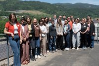Gruppenfoto im Freien: Einige Personen stehen auf einer Terrasse mit Geländer und Solarpaneelen, dahinter grüne Hügel. Sonniger Tag.