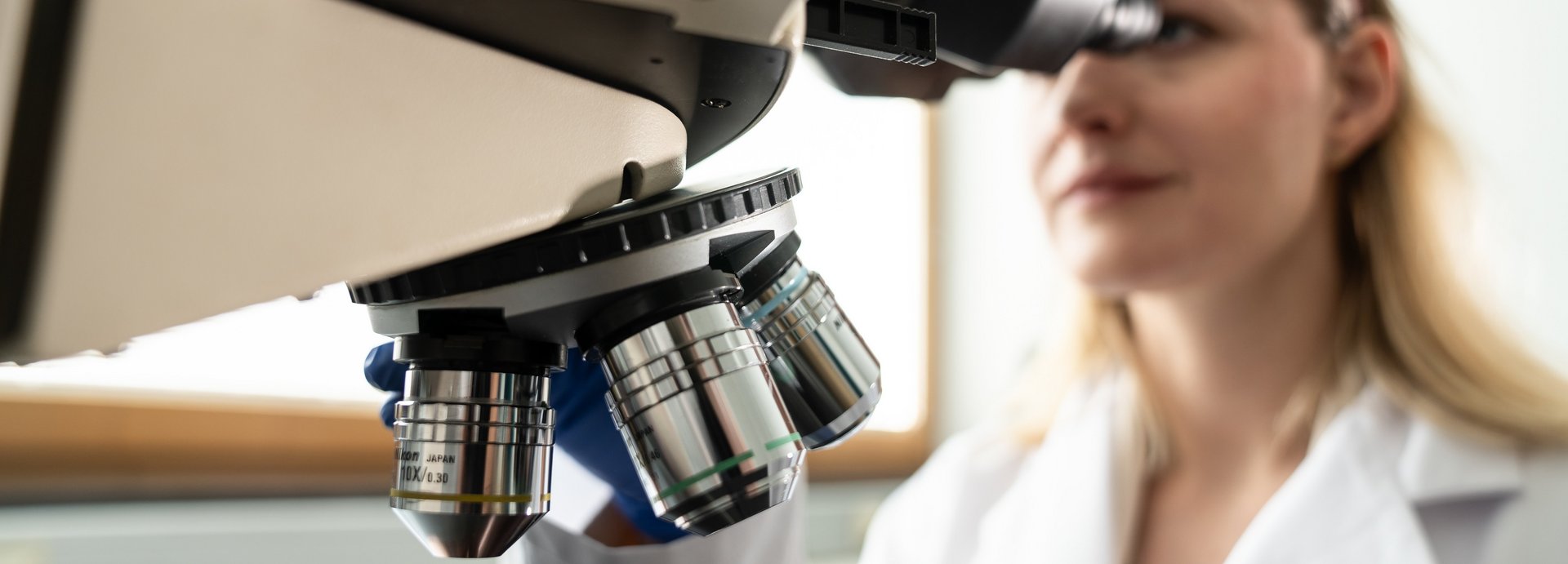 Researcher in laboratory coat in front of a microscope.