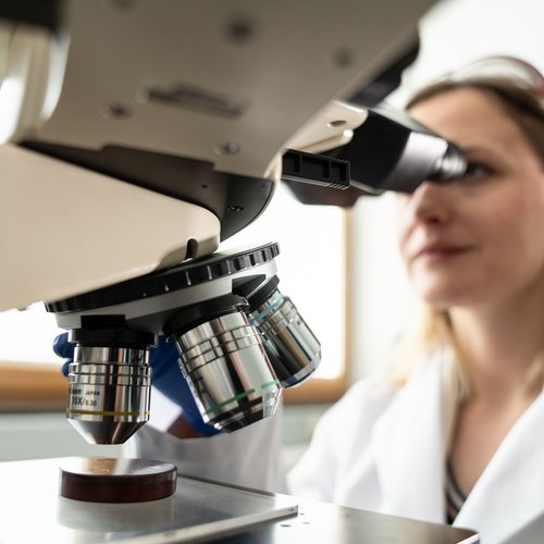 Researcher in laboratory coat in front of a microscope.