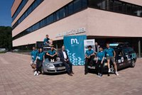 Gruppe von Personen in türkisfarbenen Shirts posiert mit zwei beklebten Autos vor dem Gebäude der Montanuniversität Leoben und einem Uni‑Banner.