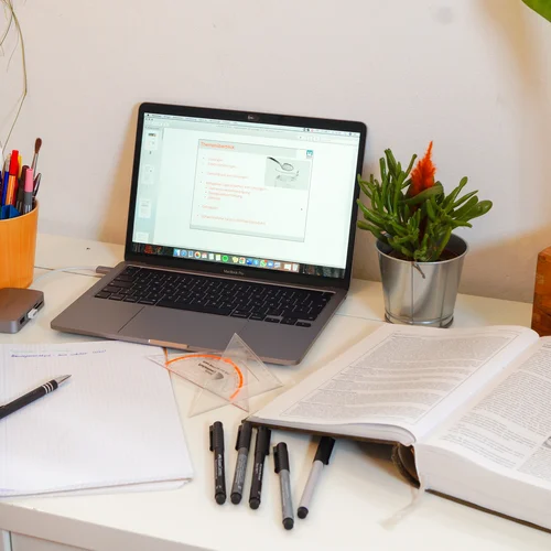 Foto: © MUL Schreibtisch mit Laptop, Büchern, Stiften, Lineal und Füße am Tisch.