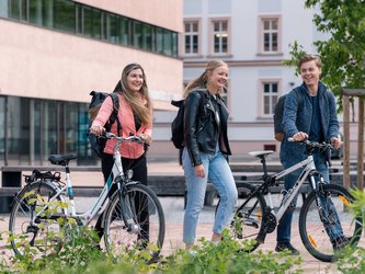 3 junge Menschen am Fahrrad vor der Universität.
