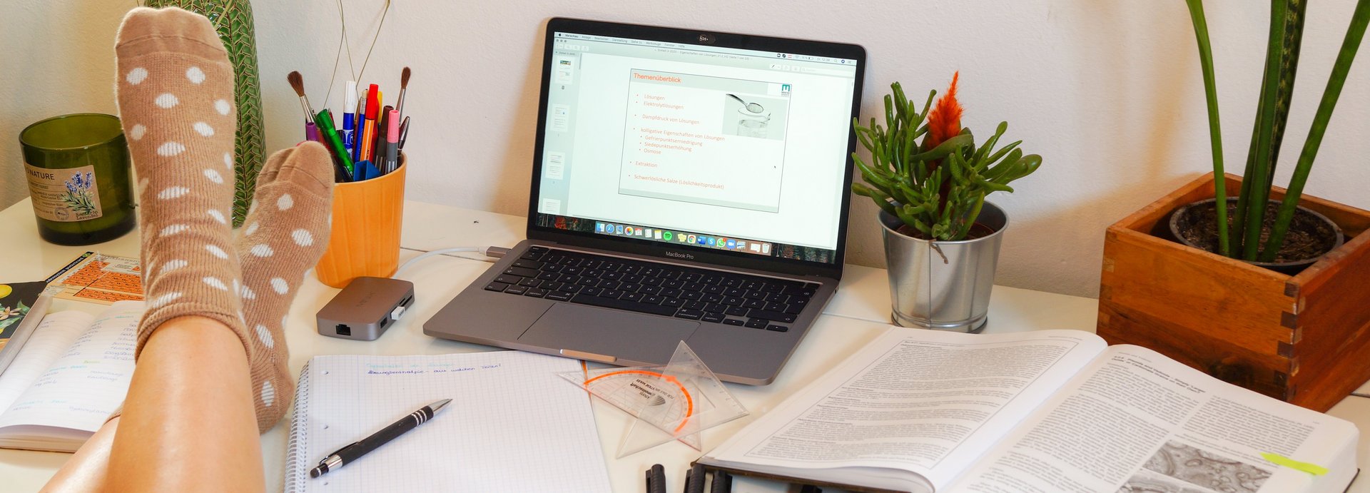 Desk with a laptop, study materials and decorations; a student has placed their feet on the desk.