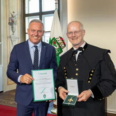 Übergabe einer Landesauszeichnung; Urkunde und Orden werden präsentiert.