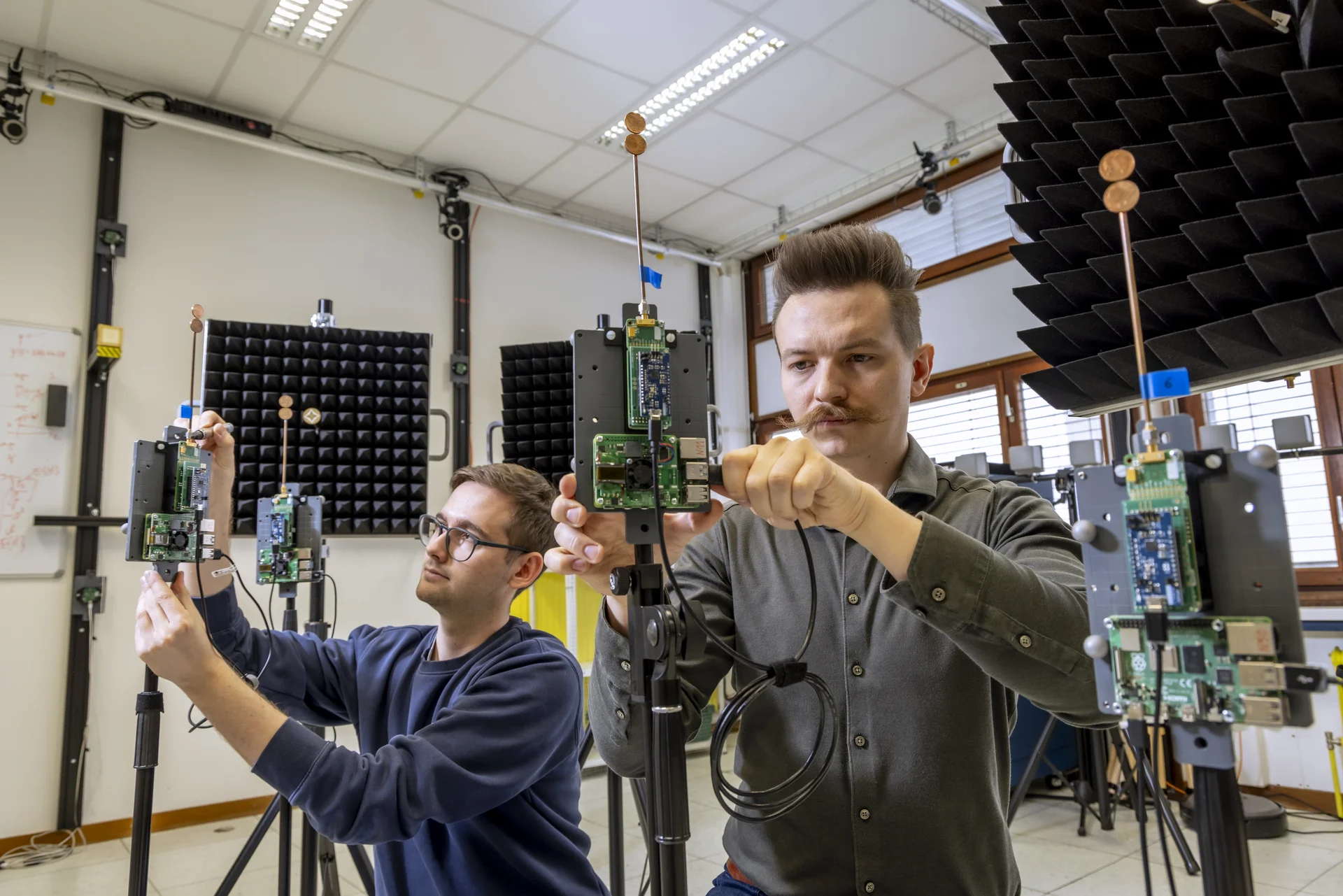 Two men are assembling devices equipped with antennas and circuit boards.