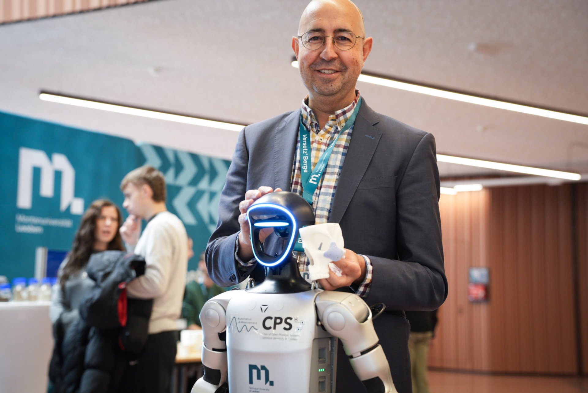 Studienberatung, Workshops und Campus-Führungen warten auf dich beim Info-Tag. Foto: © MUL Professor Bermejo steht hinter einem Roboter und lacht.