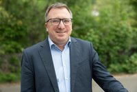 Portraitfoto, Mann mit dunklem Anzug und hellem Hemd, Brille.