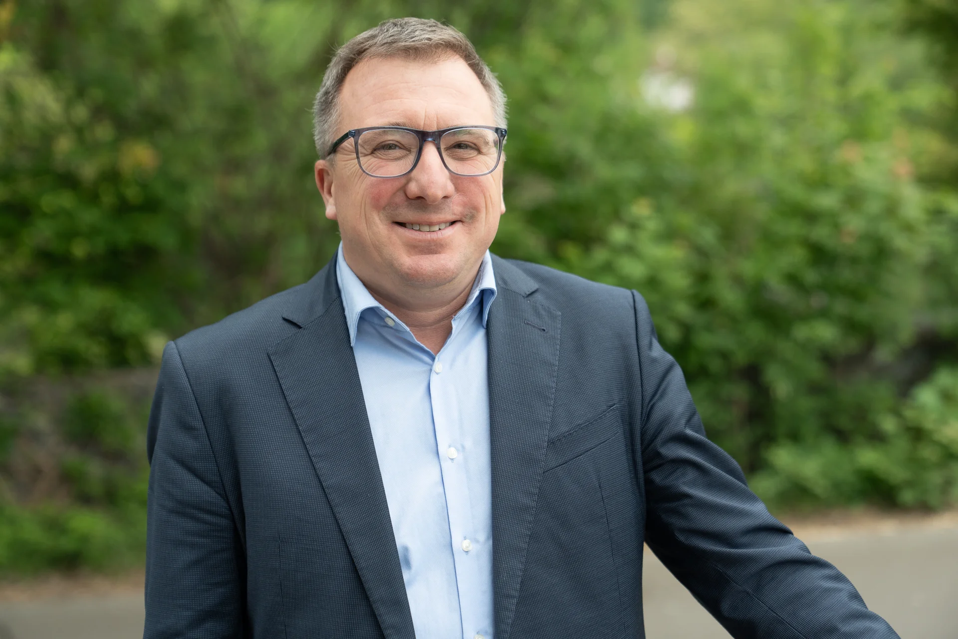 Portraitfoto, Mann mit dunklem Anzug und hellem Hemd, Brille.