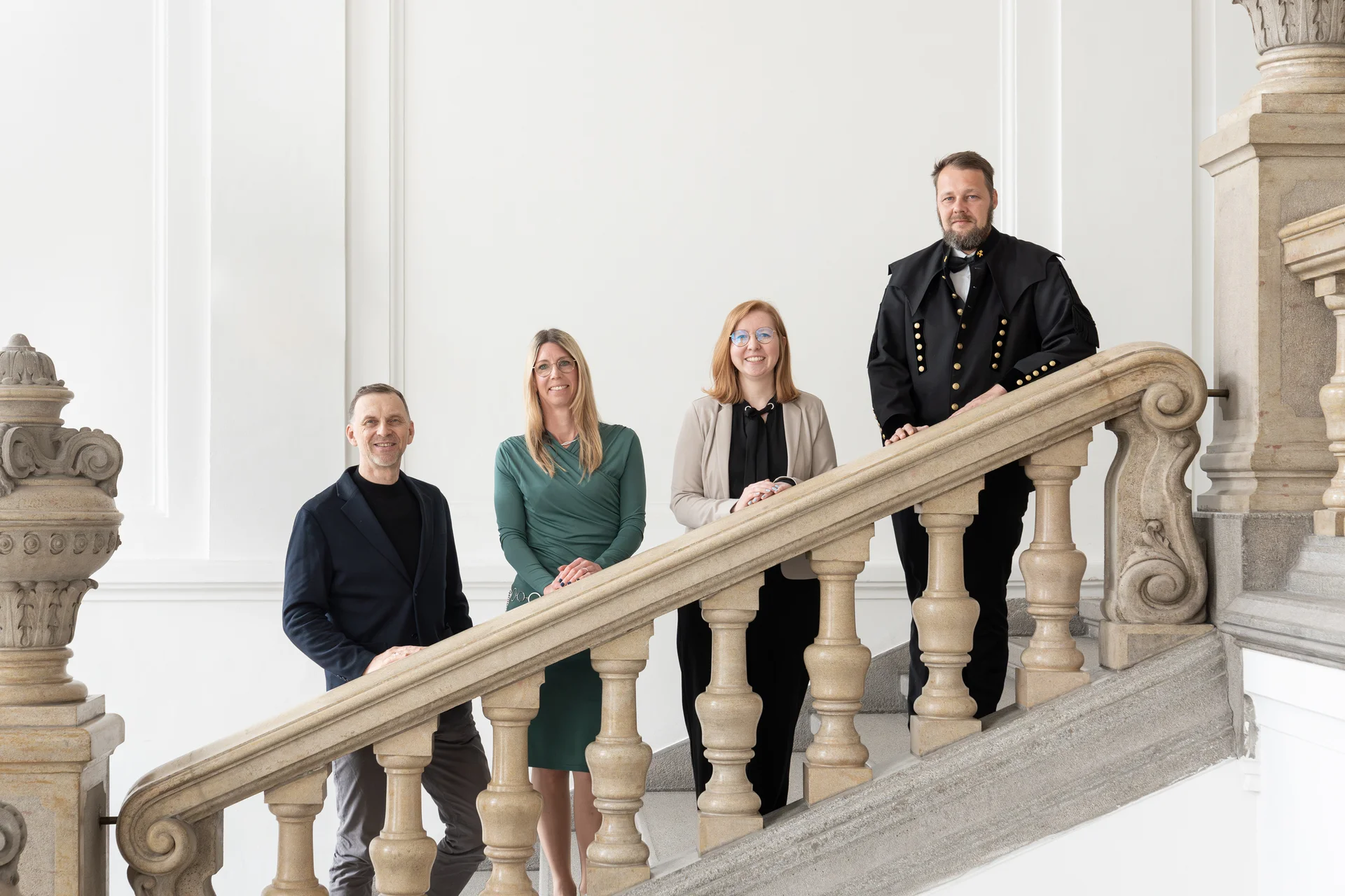 Der Universitätsprofessor steht zusammen mit den drei Habilitationsschreibern auf der Universitätstreppe.