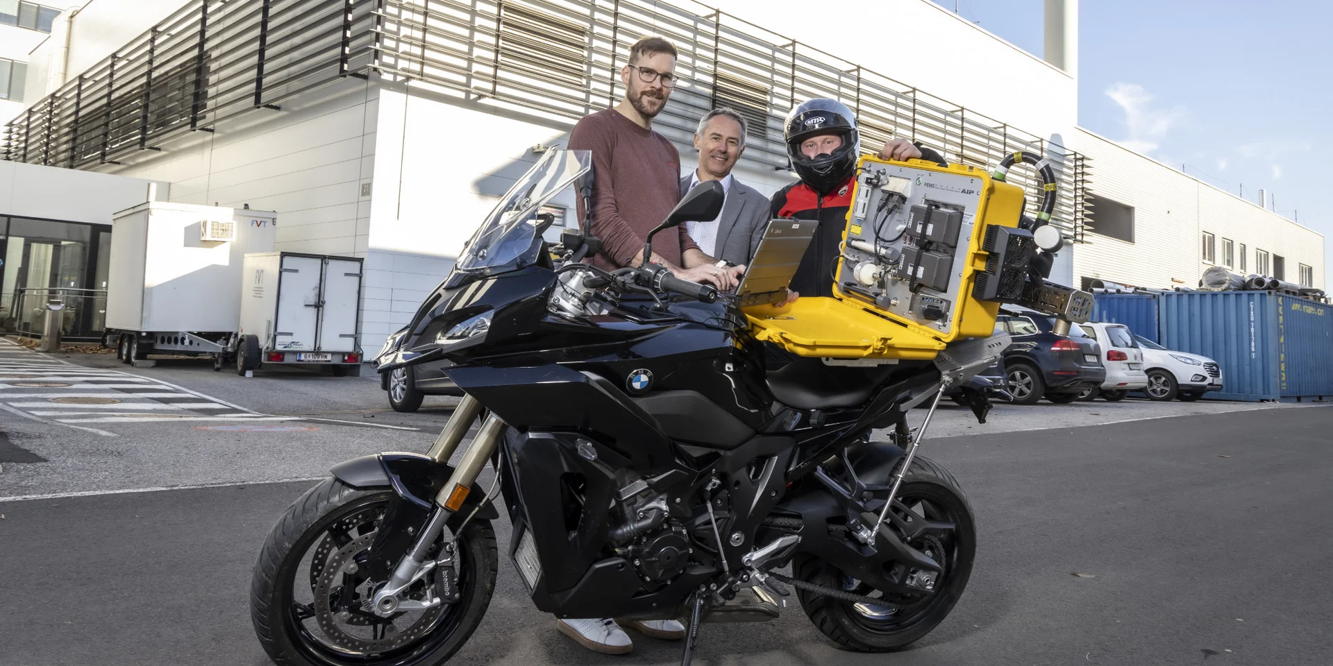 V.l.: Sebastian Schurl, Stephan Schmidt und Michael Kappel vom Institut für Thermodynamik und nachhaltige Antriebssysteme der TU Graz mit dem Emissions-Messgerät für Motorräder. Bildquelle: Lunghammer - TU Graz Drei Männer stehen hinter einem Motorrad, auf dem sich ein gelber Koffer mit einem Messgerät befindet.