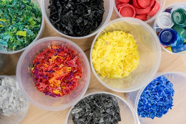 Schalen mit bunten Kunststoffschnitzeln in verschiedenen Farben, von Rot und Gelb bis Blau, Grün und Schwarz.