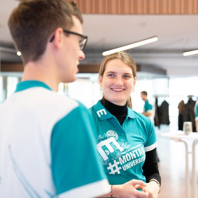 Eine junge Frau und ein junger Mann stehen zusammen und sie lächelt.