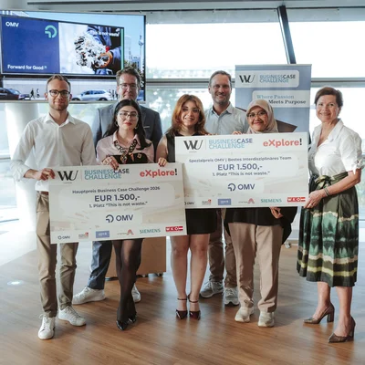 Gruppenfoto in Innenräumen: acht Personen, zwei halten große Symbol-Schecks über 1.500 €, Banner und Monitor im Hintergrund.