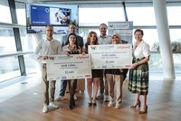 Gruppe von sieben Personen bei einer Preisverleihung an der WU; zwei Teilnehmende halten große Sieger-Schecks der Business Case Challenge mit Partner-Logos wie OMV.