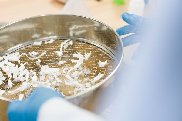 Mit Handschuhen wird zerkleinerter Kunststoff auf einem Metallsieb fraktioniert – Schritt im Recycling von Thermoplasten.