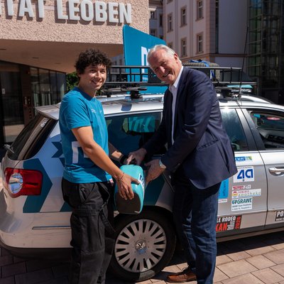 Zwei Personen betanken einen beklebten Kombi vor dem Gebäude der Montanuniversität Leoben mithilfe eines Trichters.