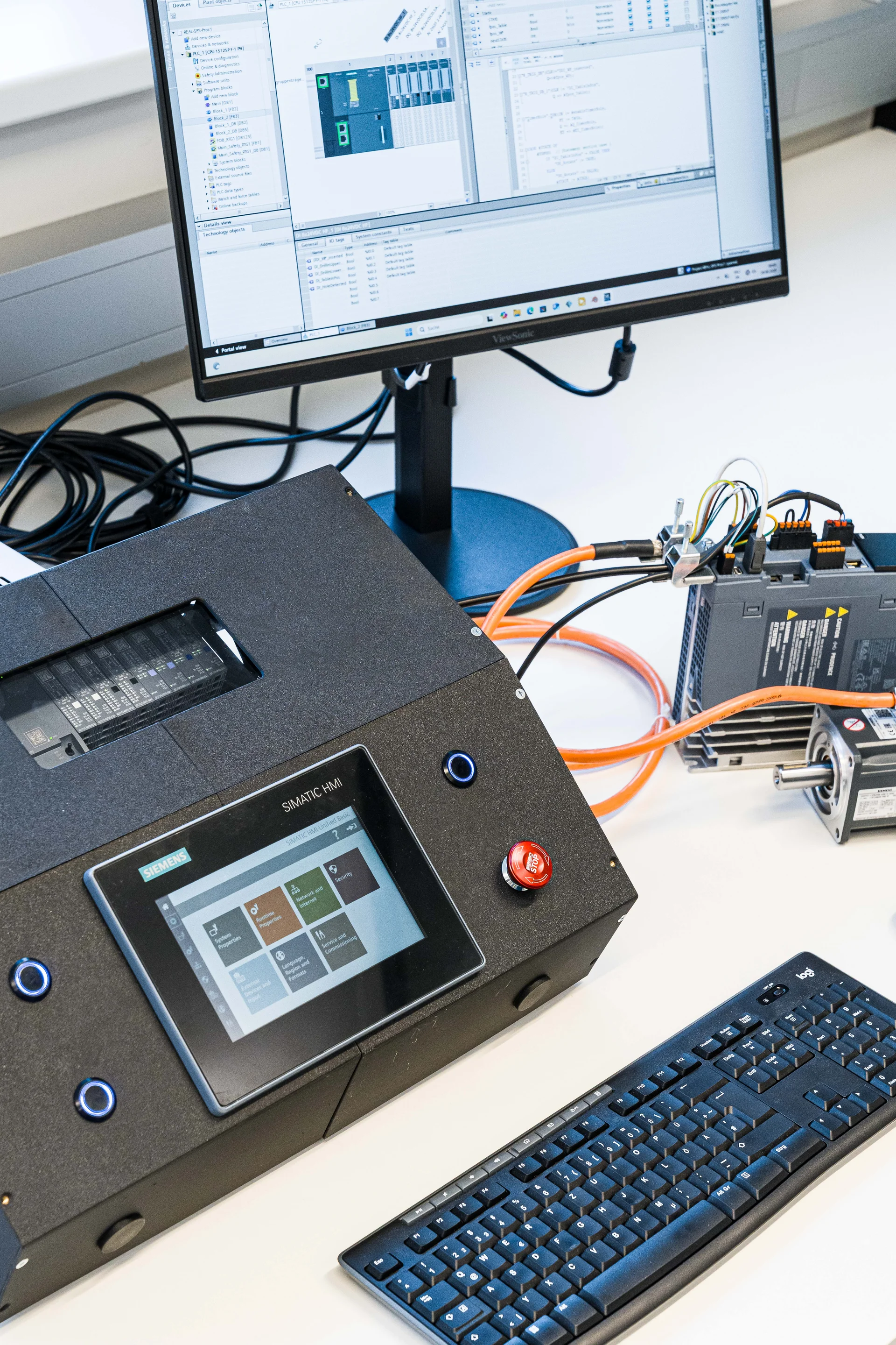 Laboraufbau zur Automatisierung: Monitor mit TIA‑Portal, HMI‑Bedieneinheit/PLC mit Touchscreen, Tastatur und verkabeltes Antriebssystem.