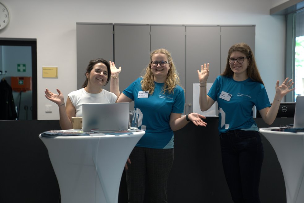Three student counsellors wait cheerfully for prospective students with their arms in the air.
