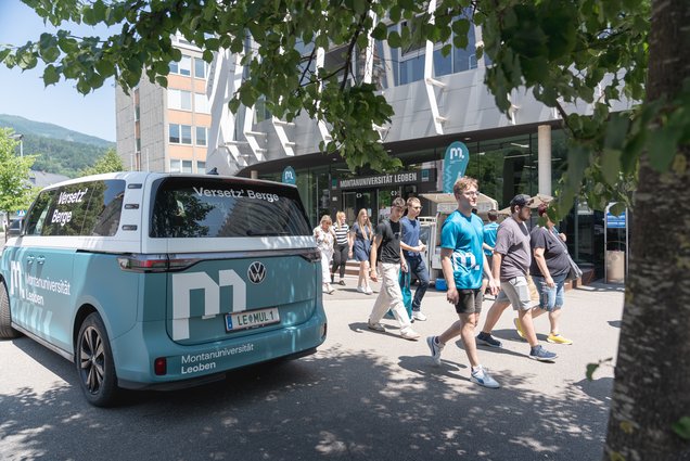 Info-Tag an der Montanuniversität Leoben. Foto: © MUL/Stefanie Luschin Gruppe von Studierenden geht vor dem Haupteingang der Montanuniversität Leoben vorbei; daneben steht ein gebrandeter Uni‑VW‑Bus.