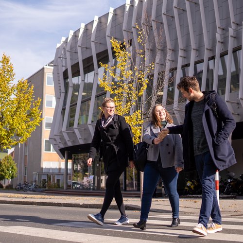 Drei Studierende verlassen den Campus und genießen den Herbst.