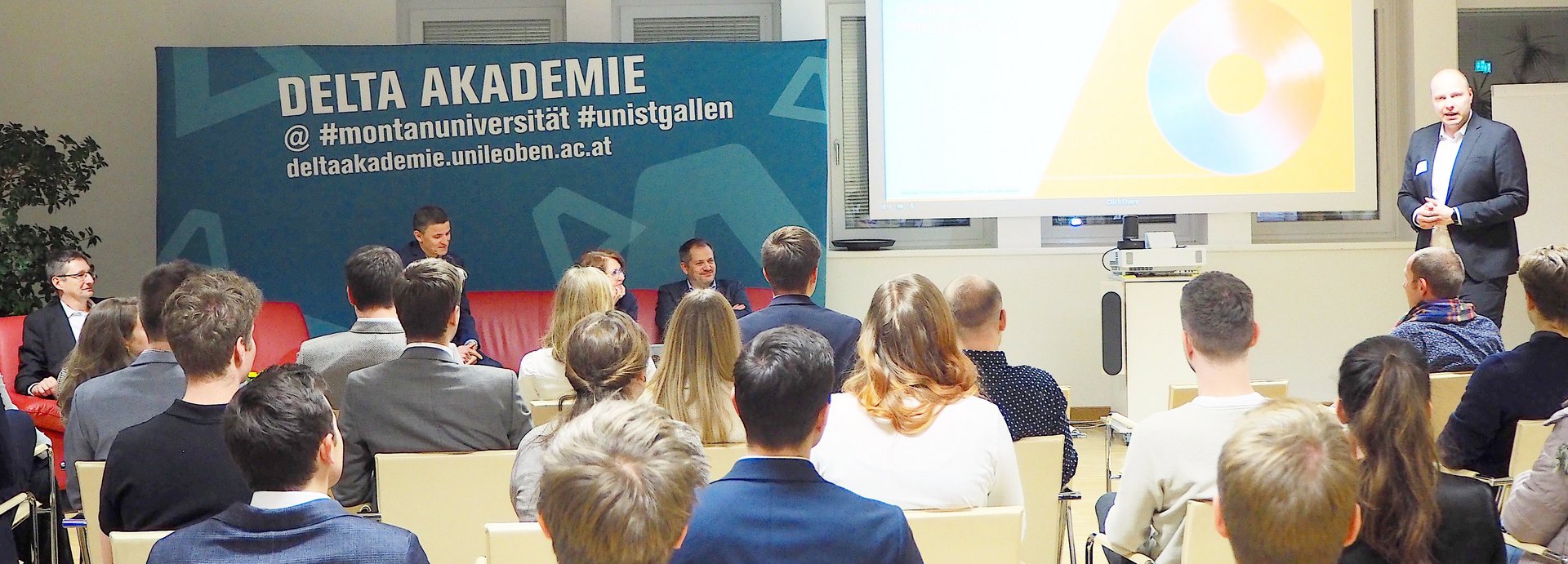 Lecturer in front of students and a poster of the Delta Academy in the background.