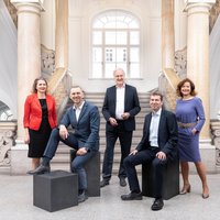 The rector and vice-rectors of the Technical University stand side by side in front of the new study centre, all smiling in their official attire. 