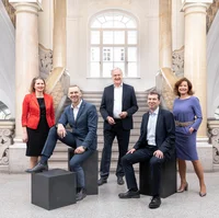 Der Rektor und die Vizerektoren der Montanuniversität stehen nebeneinander vor dem neuen Studienzentrum, alle lächelnd in offizieller Kleidung.