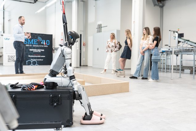 Info-Tag an der Montanuniversität Leoben. Foto: © MUL/Stefanie Luschin Roboter sitzt auf einem Transportkoffer, während ein Professor einer Studierendengruppe in einer Laborhalle etwas erklärt.