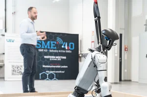 A few people are standing in a laboratory. A seated robot can be seen in the foreground.