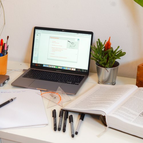 Desk with laptop, books, pens, ruler and feet at the table.