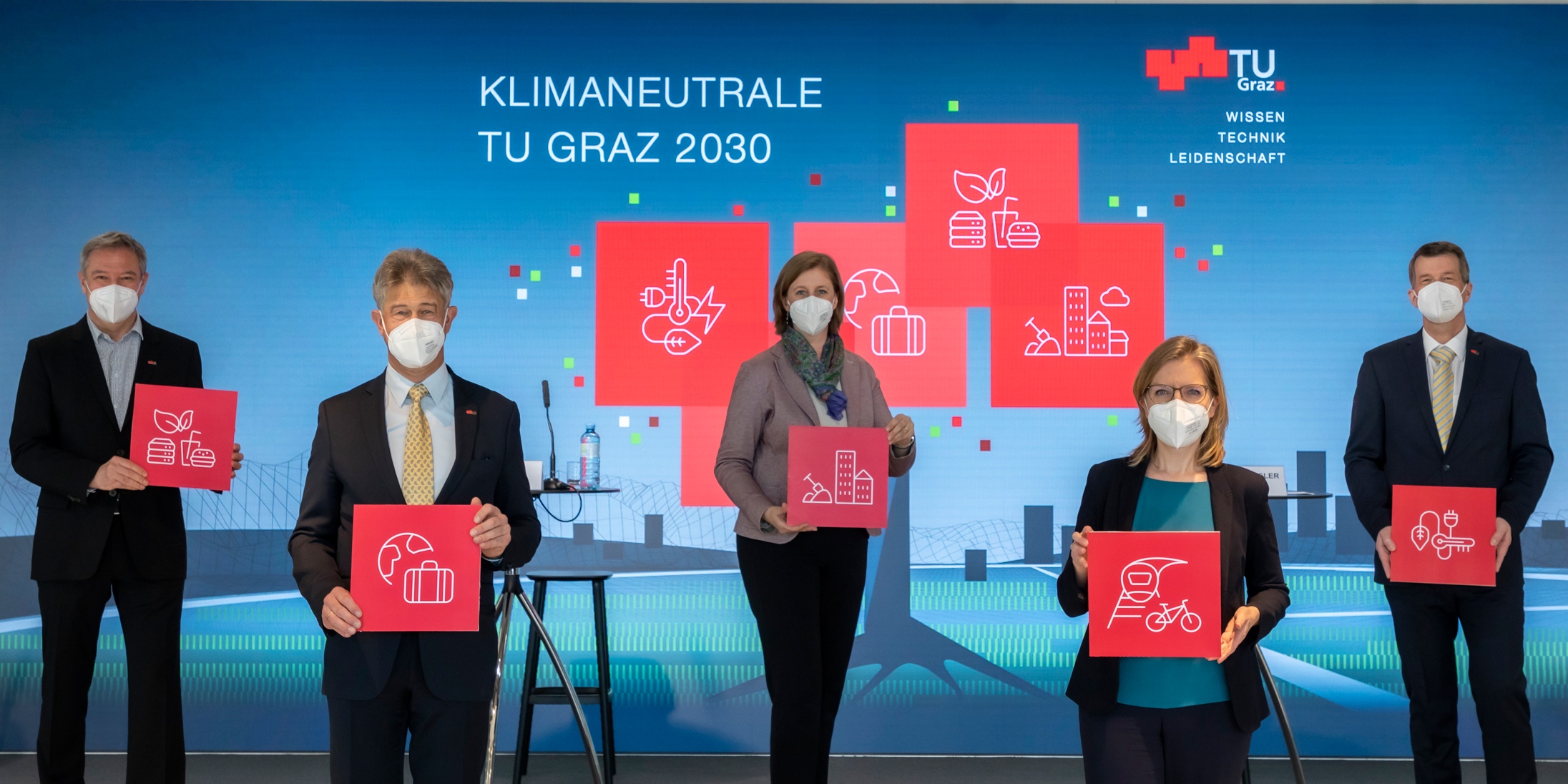 © Lunghammer – TU Graz Drei Männer und zwei Frauen mind MNS-Schutz und Tafeln vor einer LED-Leinwand