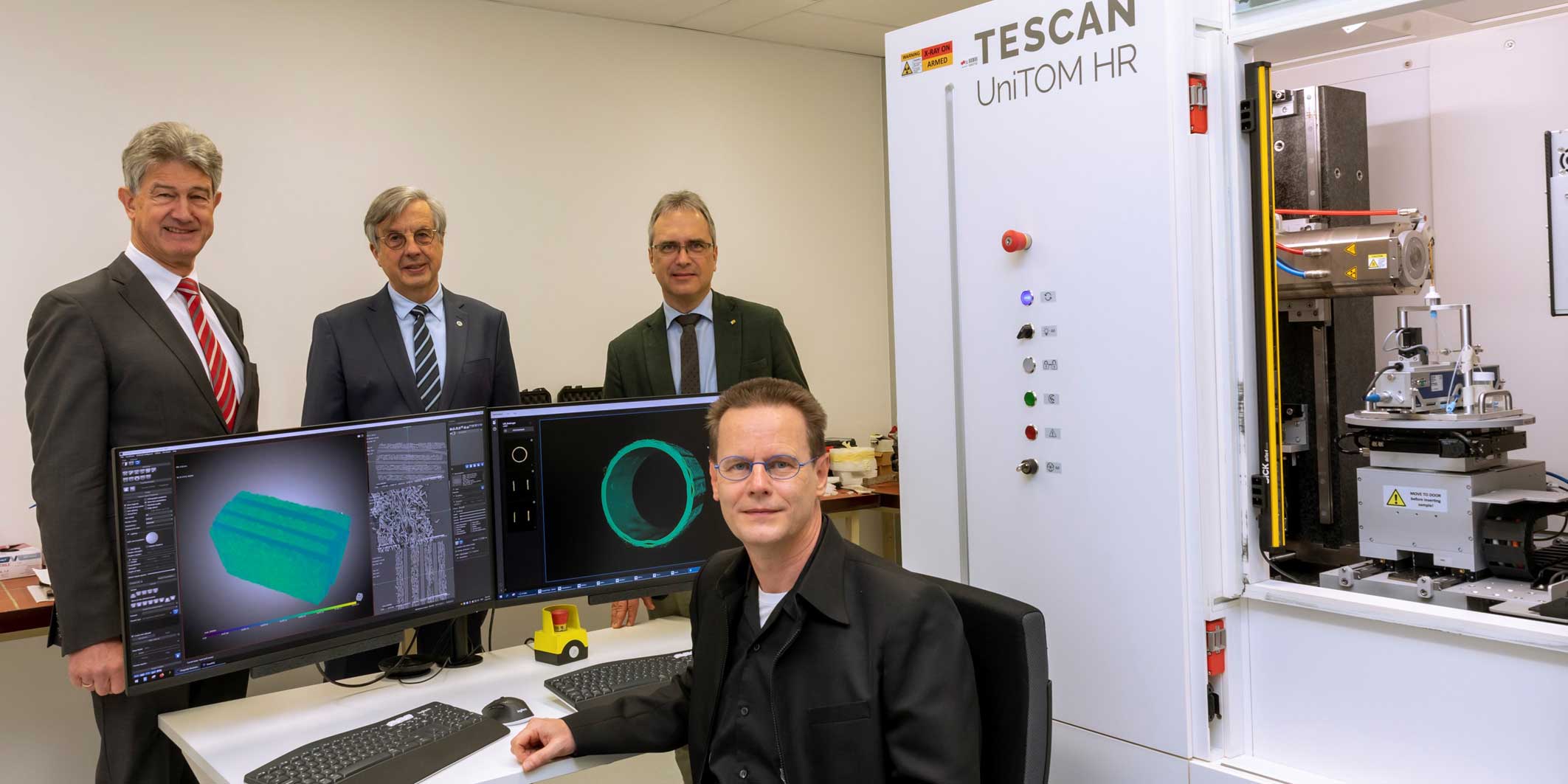 © Lunghammer – TU Graz Vier Herren neben zwei Computer-Bildschirmen und einer Micro-CT-Kammer